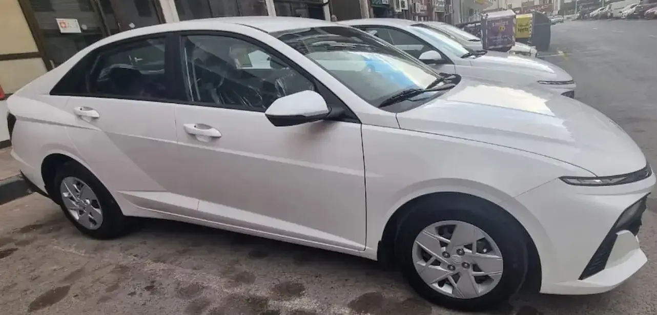 منظر جانبي لسيارة هيونداي اكسنت 2026 بيضاء اقتصادية للإيجار في أبوظبي